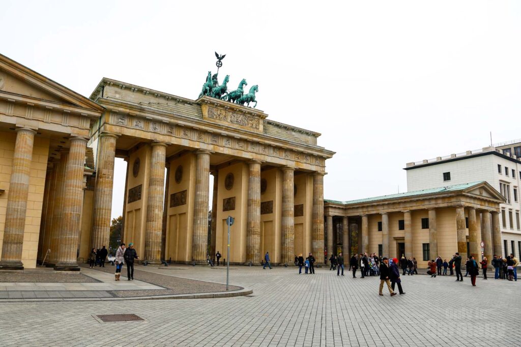 The Brandenburg Gate in Berlin during winter, people dressed in warm clothes walking by.