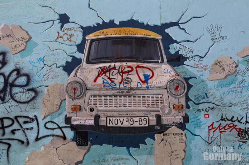 Graffiti on the Berlin Wall of a car that seems to smash through the Berlin Wall.