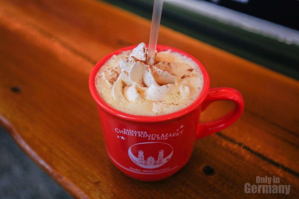 A German Christmas drink  called Schneemann punsch with cream in a red cup sitting on a wooden surface