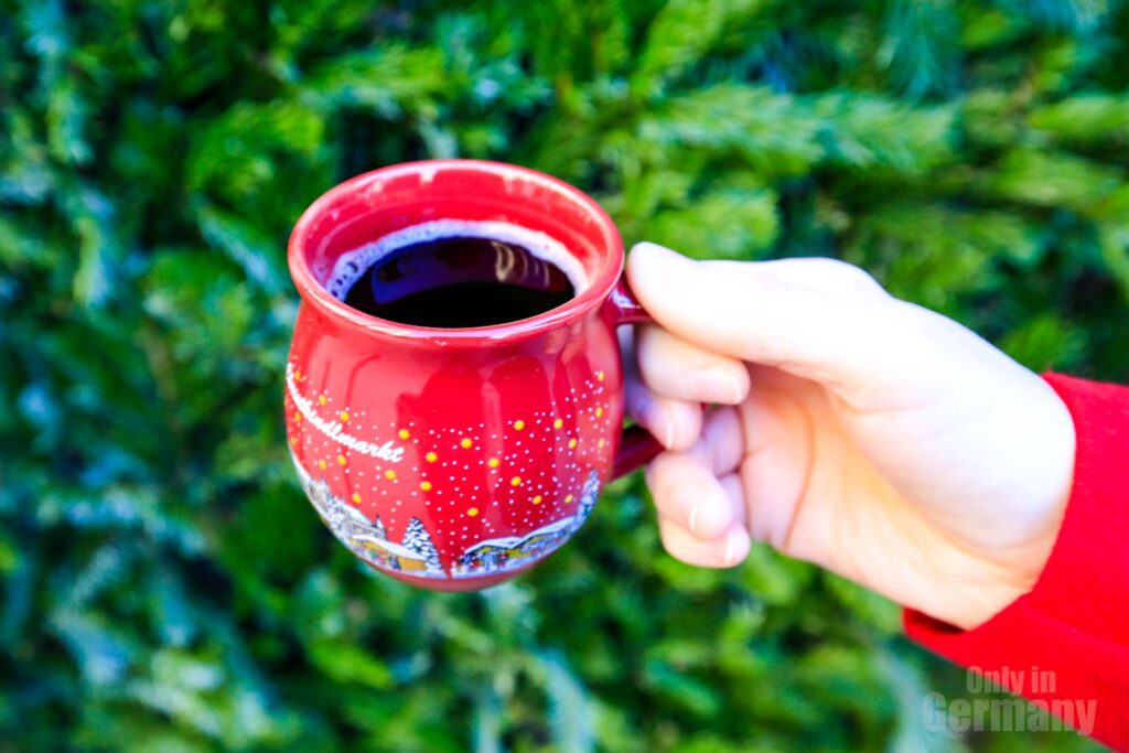 A hand holding a red mug of mulled wine in a Christmas market in Germany